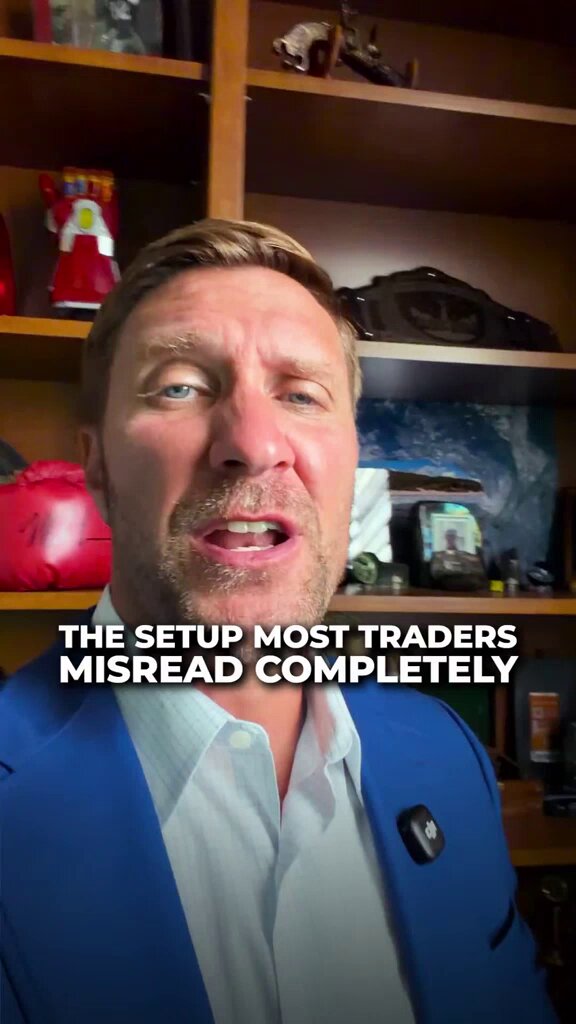 The image features a man wearing a blue suit jacket, standing against a brown background with a shelf of books behind him. The man appears to be talking about Bitcoin or cryptocurrency trading, as indicated by his attire and the context provided in the caption.