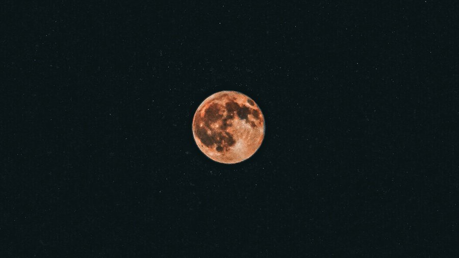 A full moon glows with a warm reddish hue against a dark, starry night sky.
