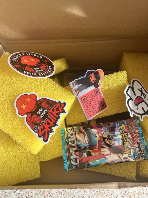 An open subscription box for 'Skullz World' containing yellow foam packaging, several character stickers, a QR code card, and a Digimon trading card pack featuring what appears to be Agumon.
