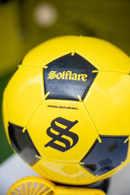 A yellow and black Solflare soccer ball with "OFFICIAL SOLFLARE BALL" text and an "S" logo rests on a stand, fitting the post's theme of selecting a winner for the day's trophy in what appears to be a Solflare-sponsored soccer event.