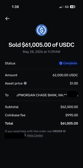 In the image, there's a black cellphone displaying a message about cryptocurrency transactions that went through a Coinbase service. The phone screen shows an auction price of $61,000 USDC for an asset priced at $62,000. A total amount of $1,000,00 USDC has been paid, along with the remaining balance of $9,999 USDC after the transaction is complete. The phone screen also includes details about how to pay the Coinbase fee through a PayPal order.