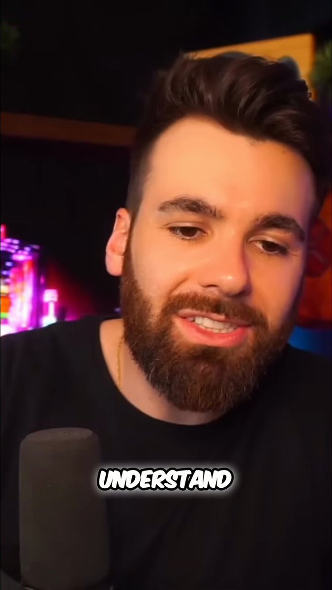 The image features a man with a beard wearing a black shirt, who appears to be talking into a microphone or speaking into an earpiece. The background of the image shows a dark room with neon lights, which suggests that this could be a recording studio or a similar environment for live broadcasts or podcasts. There is also text in the image that reads "understand", possibly indicating a theme or topic related to the man's speech or message.