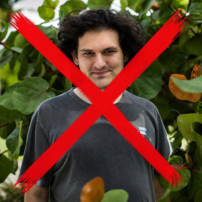 A photo of a curly-haired man in a dark t-shirt surrounded by green foliage with a large red X painted across him.