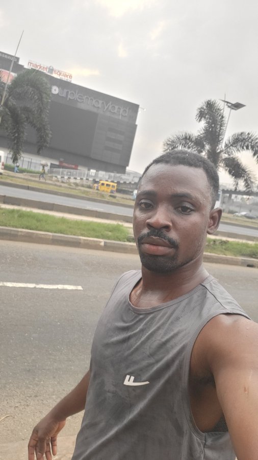 A man takes a selfie on a roadside near "market square" and "supplemenland" buildings, with palm trees and an overcast sky in the background. The caption "Another day, another chance. Sending you good energy today, mutuals" complements the contemplative selfie vibe, conveying a mood of quiet motivation amid a typical day outdoors.