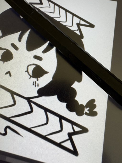 A black electronic device, possibly a drawing tablet or e-reader, resting on top of a printed illustration of a crying character with a braid.