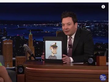 Jimmy Fallon holds up a print of his Bored Ape Yacht Club NFT #599 while seated at his Tonight Show desk, which directly illustrates the post's claim that he purchased the NFT for 217K and has never sold it despite the floor price dropping to $12,600.