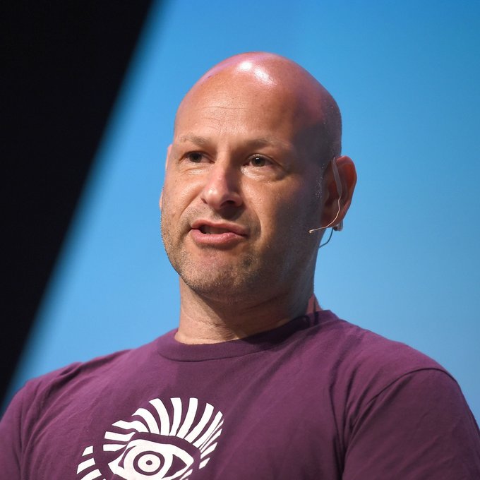 Joe Lubin, the Ethereum co-founder, speaks at an event wearing a maroon t-shirt featuring an eye logo, with a headset microphone visible, as he discusses the shift toward self-custody and stablecoins as internet-native money.