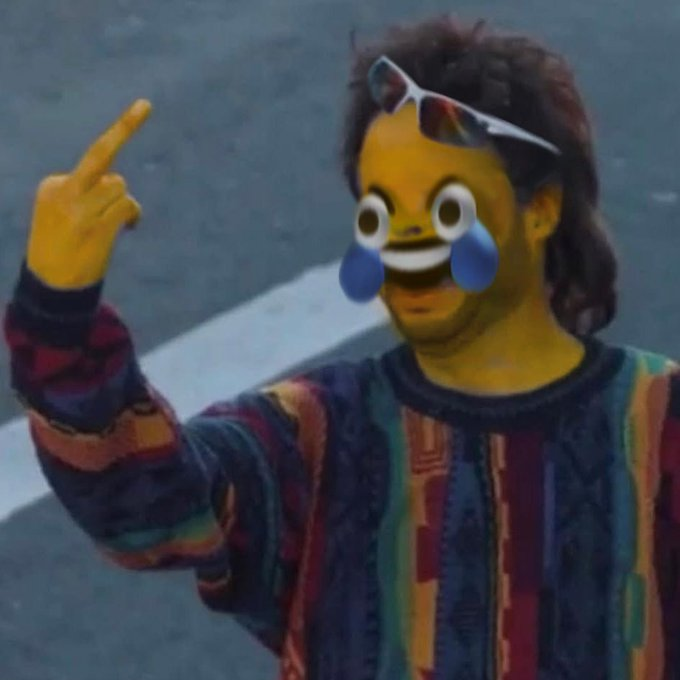 A man with long hair, sunglasses on his head, and a colorful patterned sweater points upward with a yellow emoji overlay featuring crying-laughing eyes and a wide grin pasted over his face. The meme humorously captures the forced optimism of a crypto trader greeting the day despite seeing market dips everywhere.