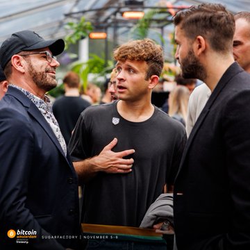 Two men in suits conversing at the Bitcoin 2024 conference at Sugar Factory on November 5-6, with a younger man in a black t-shirt listening in the middle.