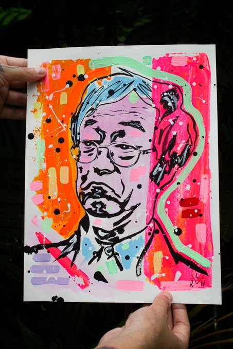 Hands holding up a vibrant pop-art style painting of a man with glasses, featuring bright pink, orange, and blue colors with paint splatter details.