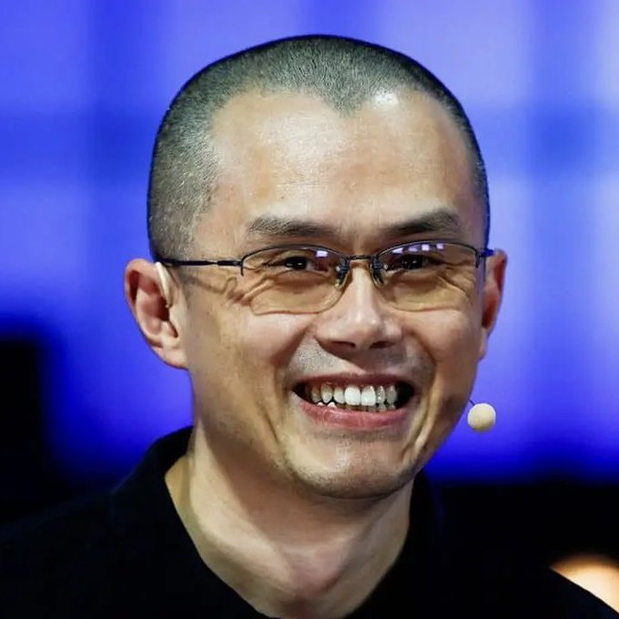 A bald man with glasses and a small headset microphone smiles broadly against a blue background, appearing to be speaking at a public event or panel. The image likely depicts Changpeng Zhao (CZ), the former CEO of Binance, visually anchoring the post's reference to his advice about building during bear markets, with ASTER DEX cited as a project currently following that strategy.
