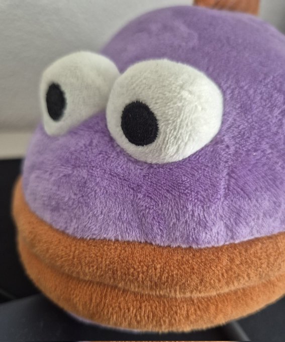 Close-up of a purple plush toy with large googly eyes sitting on an orange base.