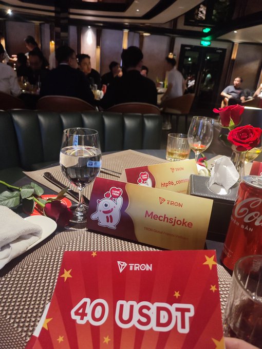 A restaurant table setup featuring TRON branded materials including a "40 USDT" coupon and a "Mechsjoke" name card for the TRON Global Premiere Event.