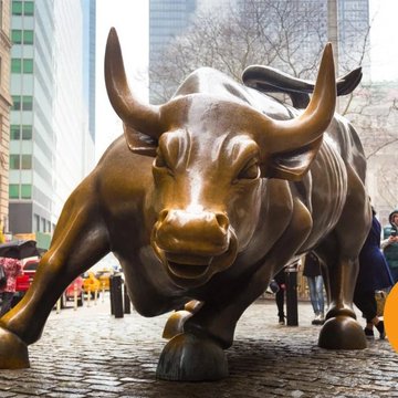 The image features a large bronze bull statue located on a cobblestone street, surrounded by people walking around. The bull appears to be charging forward or running at full speed, with its horns prominently displayed. In the background, there are tall buildings that add an urban touch to the scene. A person is holding an umbrella in the foreground, possibly indicating recent rain or strong sunlight. The post accompanying this image reads "BIGGEST BITCOIN BULL RUN EVER COMINGggG BUY THE DIPPPPPPPP". This suggests that there might be a bull statue running down the street and encourages people to buy it as part of an event or promotion.