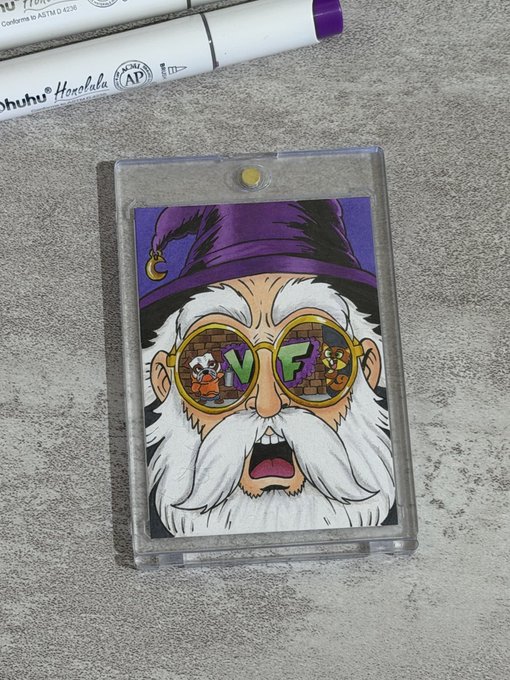 A clear acrylic badge holder containing a cartoon illustration of a wizard with round glasses that read 'V F' (with cartoon characters inside the lenses), resting on a gray surface next to a purple marker.