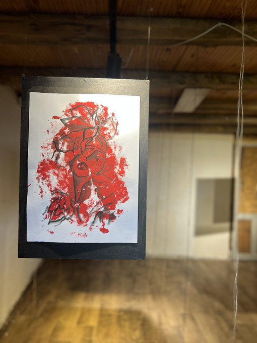 An abstract painting featuring red and black ink/mixed media on white paper, hung as artwork in a wooden interior space.