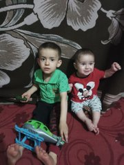 Two young children, a boy in green and a girl in red, sit together on a red rug with a small toy between them, smiling at the camera. The tender family scene reflects the post's emotional reflection on loss and gratitude, as the author shares how Web3 provided a lifeline after losing their family during the war.