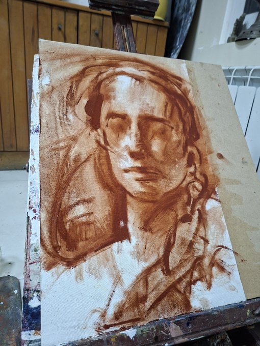 A monochromatic brown-toned underpainting of a human face on a canvas, displayed on an easel in an artist's studio.