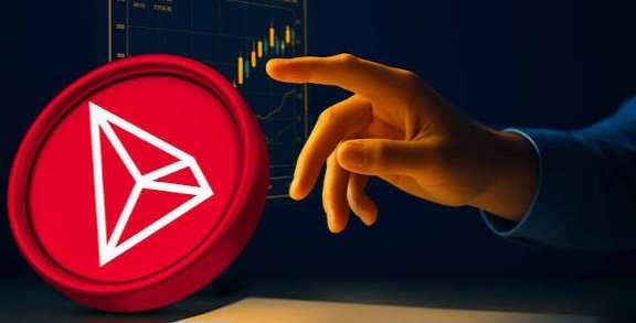 A hand reaches toward a large red Tron (TRX) cryptocurrency coin, with a trading chart visible in the background.