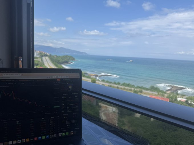 A laptop displaying financial charts and a "Closed price (June 1)" indicator sits in front of a stunning ocean view, perfectly capturing a remote work setup while the post greets followers with "GM everyone $FERRE."