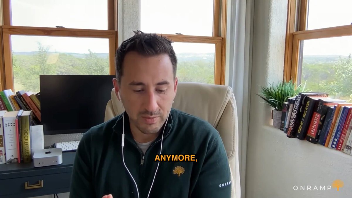 The image shows a man sitting at a desk with headphones on, possibly listening to music or participating in an online meeting. There are several books scattered around him, indicating that he might be working from home or studying. The background features a window overlooking a field, providing a view of nature outside the room. The post about inflation and assets is related to the man's situation as it suggests that his current job may not provide him with financial security in the long run due to rising costs and asset appreciation.