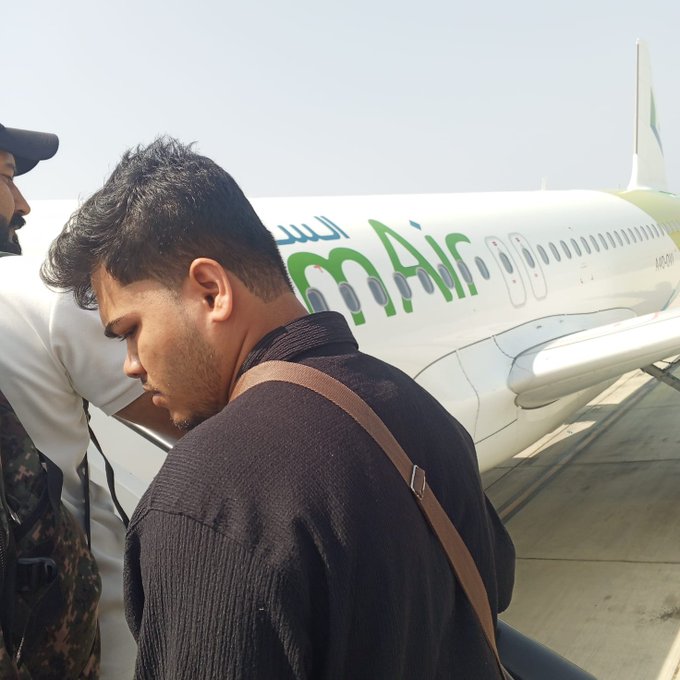 A young man with a brown shoulder bag stands in front of a Bm Air airplane.