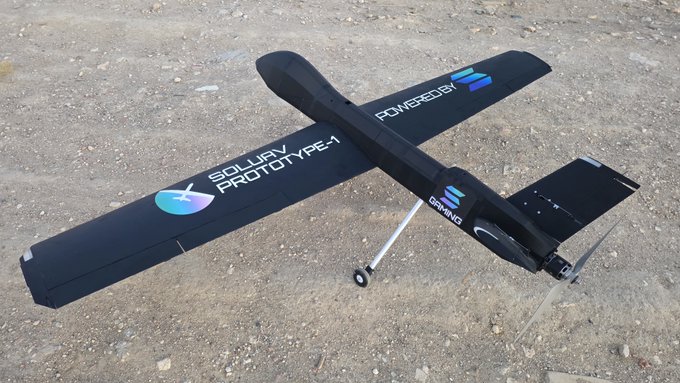 A black fixed-wing RC airplane labeled 'SOLWAY PROTOTYPE-1' and 'POWEREDBY' sits on a gravel surface, equipped with a small propeller and landing gear.