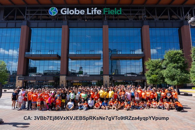 A large group photo taken in front of Globe Life Field, featuring many people mostly dressed in orange, with a contract address "CA: 3VBb7Ej86VxKVJEBSpRKsNe7gVTo9tRZza4yqpYVpump" displayed at the bottom.
