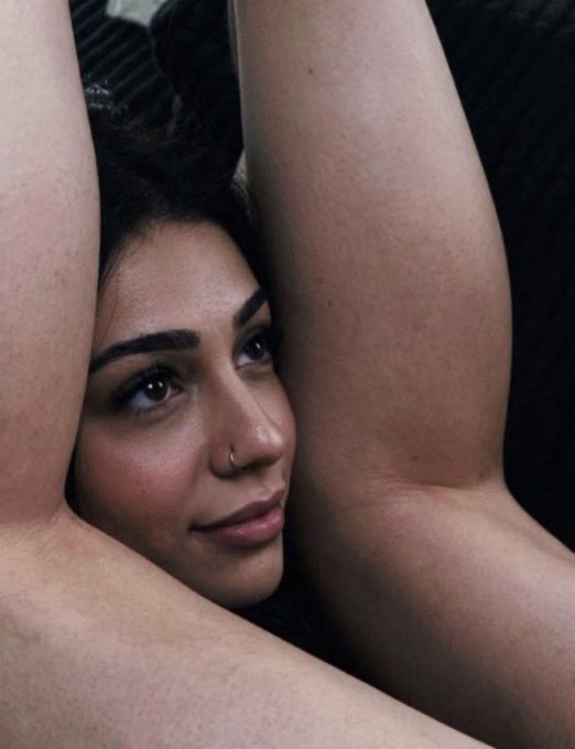 The image features a close-up portrait of a woman with dark hair, a nose ring, and well-defined eyebrows, gazing intensely while framed between her raised arms. The contemplative, soulful expression complements the post's humorous caption about a skeptical reaction to someone whose entire net worth is invested in Bitcoin.