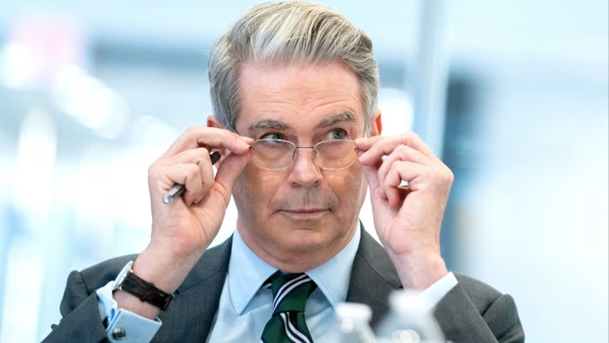 Scott Bessent adjusts his glasses while listening during a meeting. The image relates to the post showing the US Treasury Secretary commenting on the crypto Clarity Act being at the "1-yard line" of being passed.