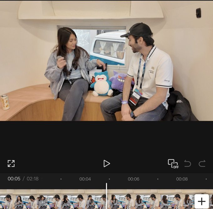 A video player interface showing an interview scene with a young woman and a man wearing a 'Wuthering Waves' lanyard sitting inside a small room, with the video timestamp at 00:05/02:18.
