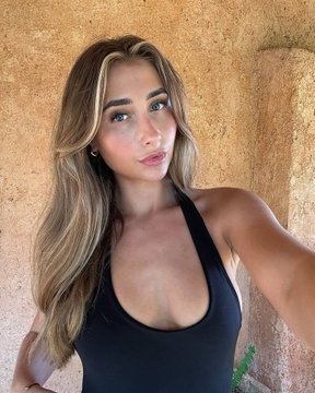 A young woman with long blonde hair wearing a black athletic top poses against a textured stone wall, appearing to be a selfie-style photo. The image appears to be used as a visual representation of "Bonnie Blue" referenced in the accompanying post about a Polymarket prediction leaderboard.