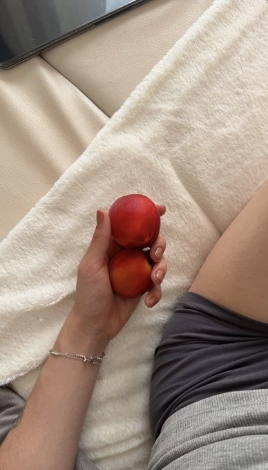 A person's hand holding two red nectarines/plums while lying on a white textured blanket or couch.