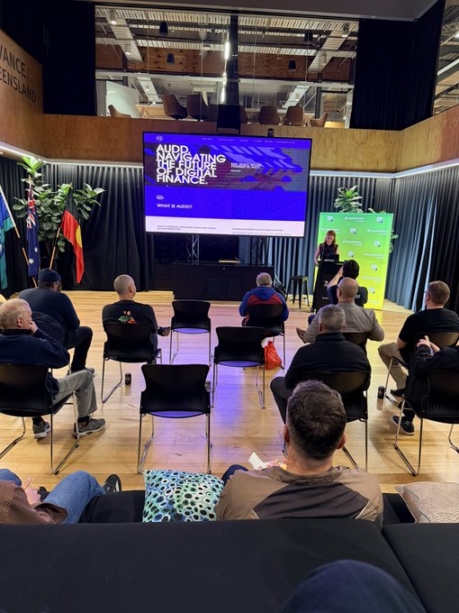 An audience seated at an event titled 'NAVIGATING THE FUTURE OF PERSONAL FINANCE' with 'WHAT IS RWA?' displayed on a large screen, with a speaker presenting near the stage.