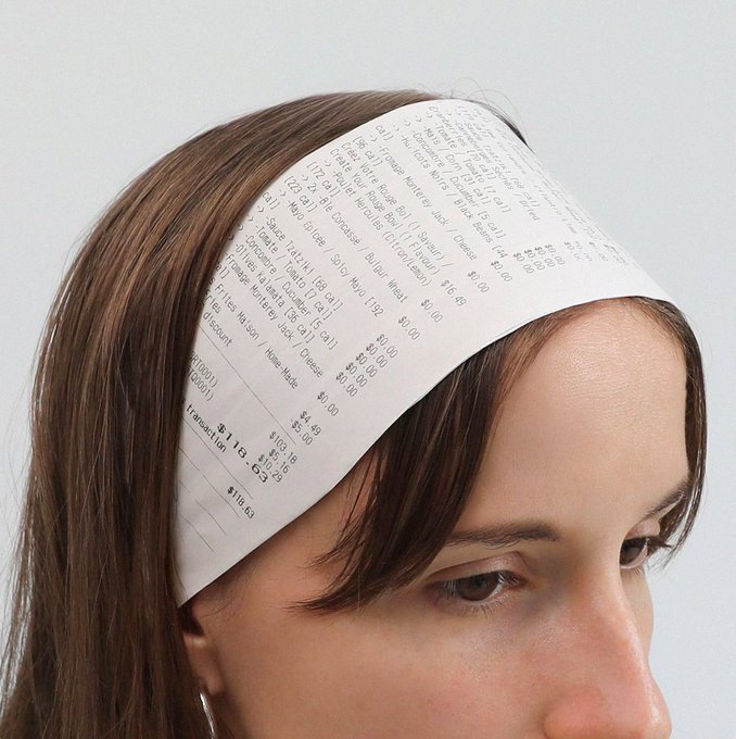 A close-up of a woman with a printed receipt taped to her forehead, listing items and prices like 'Subtotal $69.00' and 'Transaction $115.50' with a total of $100.63.