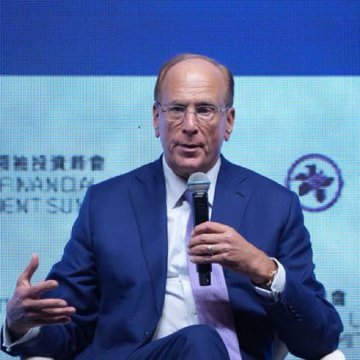 A man in a blue suit and glasses speaking into a microphone, with 'FINANCIAL' and 'SUPERVISION' text visible on a screen behind him.