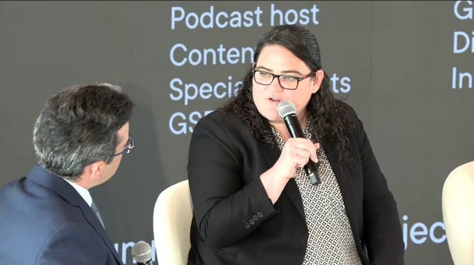 A woman with glasses speaks into a microphone at a panel event; the background lists roles including 'Podcast host' and 'Content' and 'Specialist'.