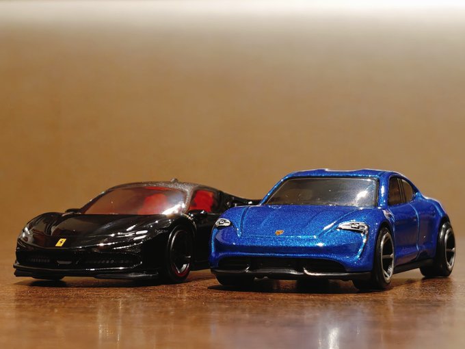 Two toy sports cars, one black Ferrari and one blue Porsche, sitting on a wooden surface.