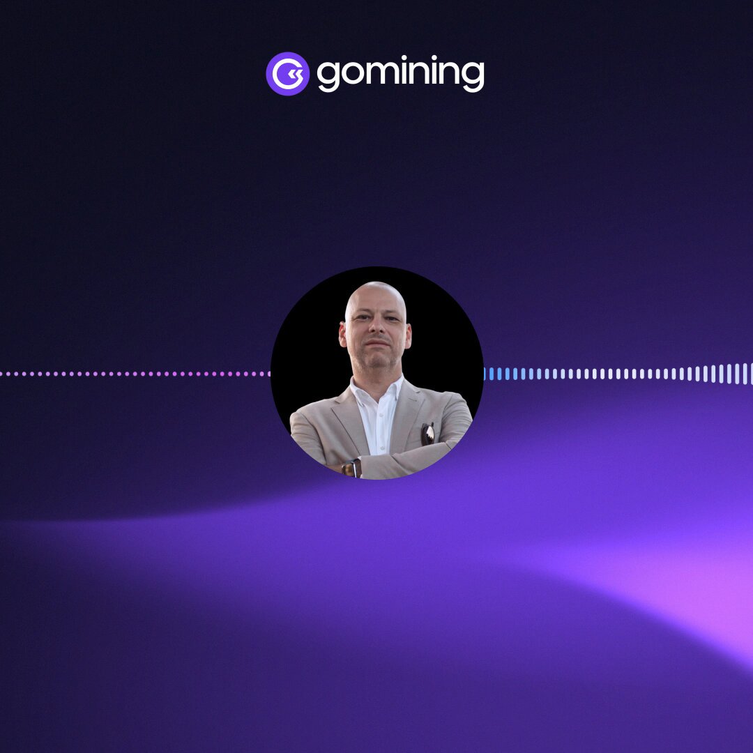 The image features a man wearing a suit standing against a purple background with white lines. The man has his arms crossed over his chest, giving him an air of confidence or authority. The image does not provide any specific information about Bitcoin mining or the Gomining platform.