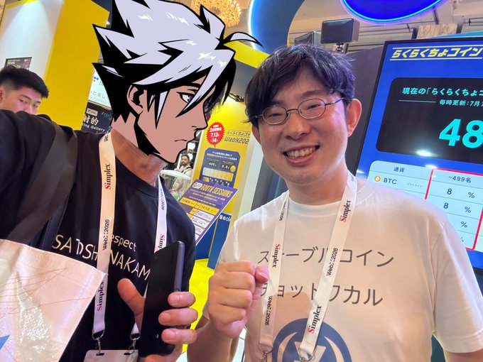 A smiling man wearing glasses and a "スープリックoin" T-shirt poses next to an anime cardboard cutout of Takashi from Worst at the WebX2025 booth, with a background screen displaying "らくらくスマホ" and a BTC rate chart showing "499名."