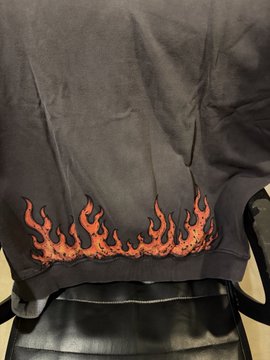 A dark gray t-shirt draped over a black office chair, featuring a vibrant orange and red flame graphic embroidered or printed along the lower back hem.