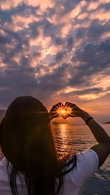 The image features a woman with long brown hair wearing a white shirt, holding her hands together in front of her face as if she's making a peace sign or a heart shape. The background shows a beautiful sunset over water, creating a serene atmosphere. The photo is captioned "Good Evening X mutuals Let make it count @quipnetwork", which suggests that the image might be related to a social media post promoting positivity and unity among mutual friends.

The woman's pose with her hands in front of her face adds a sense of connection and togetherness, reflecting the theme of the captioned image. The sunset over water serves as a stunning backdrop for this heart-shaped gesture, enhancing its visual impact and reinforcing the message of love and friendship.