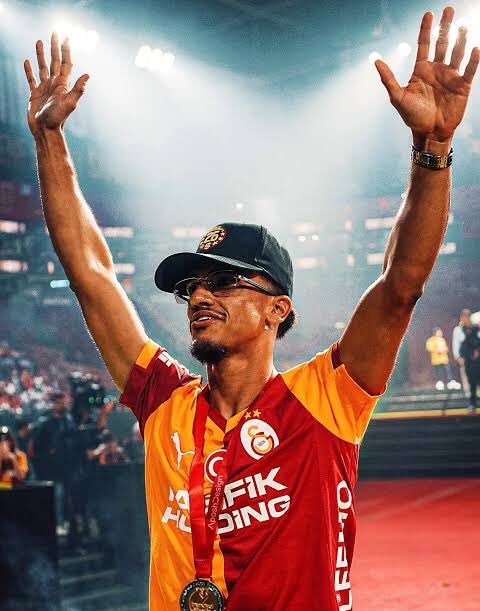 The image features a man wearing an orange and red shirt, with his arms raised high above his head as if he has just won something or achieved a great accomplishment. He is standing in front of a crowd at a sports event, which suggests that this could be a formal gala or award ceremony for the sport. The post caption reads "Gala", indicating that the image was taken during an event with a formal dress code and atmosphere.

The man's attire includes a red shirt and a black cap, adding to his celebratory appearance. He is also wearing glasses, which further emphasizes his victory or achievement.