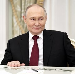 Russian President Vladimir Putin is pictured in a formal dark suit with a maroon tie, seated at a desk in what appears to be an official setting. The image accompanies the breaking news that Russia, under his administration, is advancing with MOEX's launch of Bitcoin and crypto trading on December 1, signaling a major policy direction in contrast to U.S. regulatory delays.