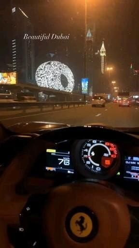 The image shows a car's dashboard with various gauges and controls, including speedometer, fuel gauge, and odometer. The car appears to be a sports car or luxury vehicle, as indicated by its design and features. In the background, there is a cityscape featuring tall buildings, which could be Dubai, as suggested by the caption provided.