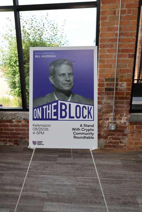 A promotional sign displayed on an easel announces Congressman Bill Huizenga's "On the Block: A Stand With Crypto Community Roundtable" event in Kalamazoo on 08/25/26 at 4-5PM, marking the conclusion of the third stop on the Stand With Crypto community roundtable tour focused on digital assets.