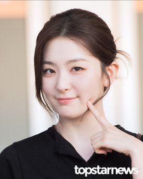 A close-up portrait of a smiling young woman with her hair pulled back, posing with her hand gently on her cheek, wearing a black top with "topstarnews" visible in the corner. The post's reference to a "mother of all GLs" suggests she may be cast in a highly anticipated 2027 girls' love drama.