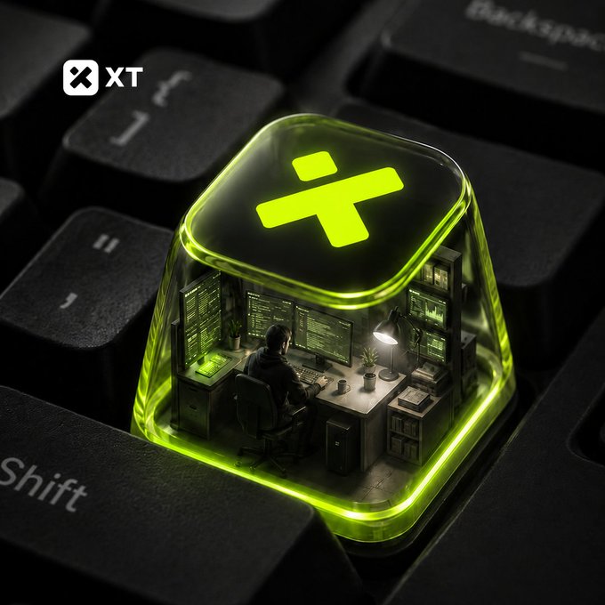 A glowing green keycap marked "XT" sits on a black keyboard and contains a miniature workspace where a developer codes at multi-monitor setup. The illuminated "XT" icon and surrounding "Shift" and "Backspace" keys visually represent the dedication of the BUIDLers powering the #XTexchange platform.