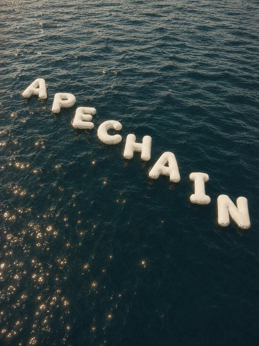 White inflatable letter balloons spelling 'APECHAIN' floating on dark blue sparkling water, illuminated by sunlight reflecting off the surface.