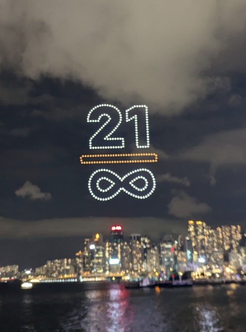 A nighttime cityscape with a watermark reading '21 ∞' over the buildings and water.